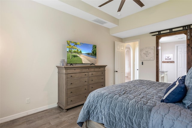bedroom with a ceiling fan, visible vents, arched walkways, wood finished floors, and baseboards