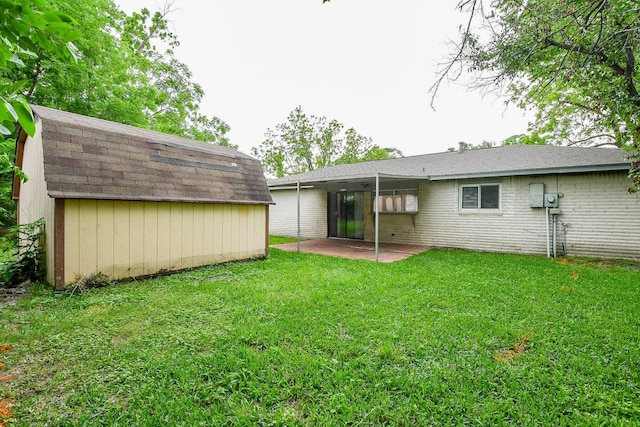 rear view of house featuring an outdoor structure, a shed, a yard, a patio, and a shingled roof