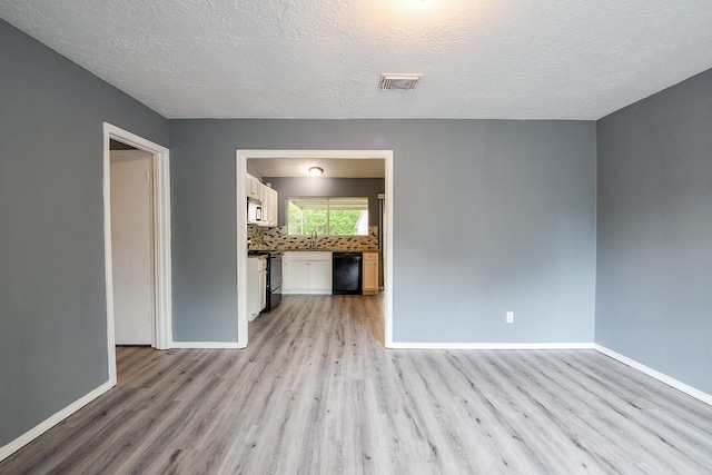 spare room with a sink, light wood finished floors, a textured ceiling, baseboards, and visible vents