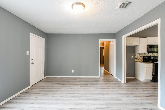 unfurnished living room featuring baseboards, a textured ceiling, visible vents, and light wood-style flooring