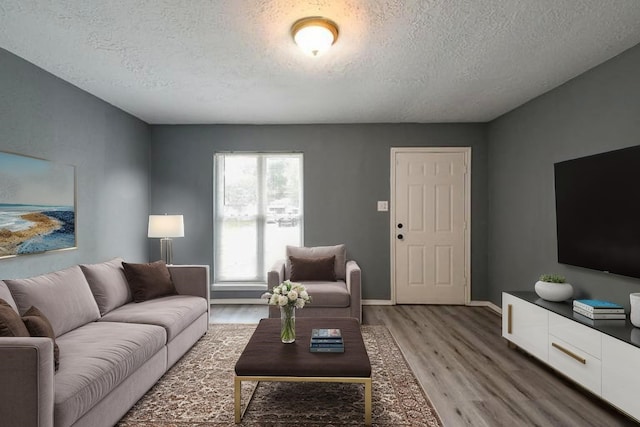 living room featuring light wood-style floors, baseboards, and a textured ceiling