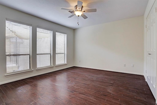 unfurnished room with dark wood-type flooring, a ceiling fan, and baseboards