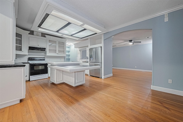 kitchen with white cabinets, stainless steel fridge, light wood finished floors, arched walkways, and range with electric cooktop