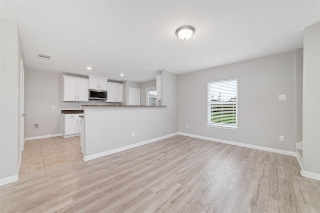 kitchen with dark countertops, white cabinets, stainless steel microwave, and light wood-style flooring