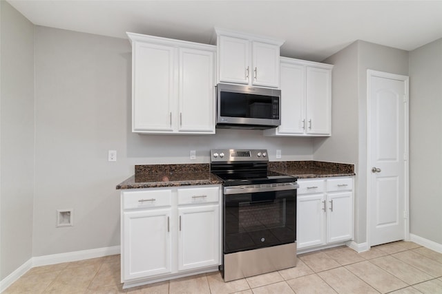 kitchen with light tile patterned flooring, baseboards, white cabinetry, dark stone countertops, and appliances with stainless steel finishes