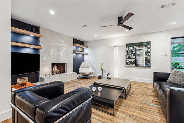 living room featuring ceiling fan, a premium fireplace, wood finished floors, and visible vents