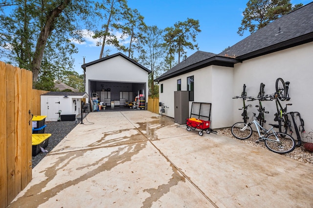 exterior space featuring fence, a shingled roof, a detached garage, stucco siding, and an outdoor structure