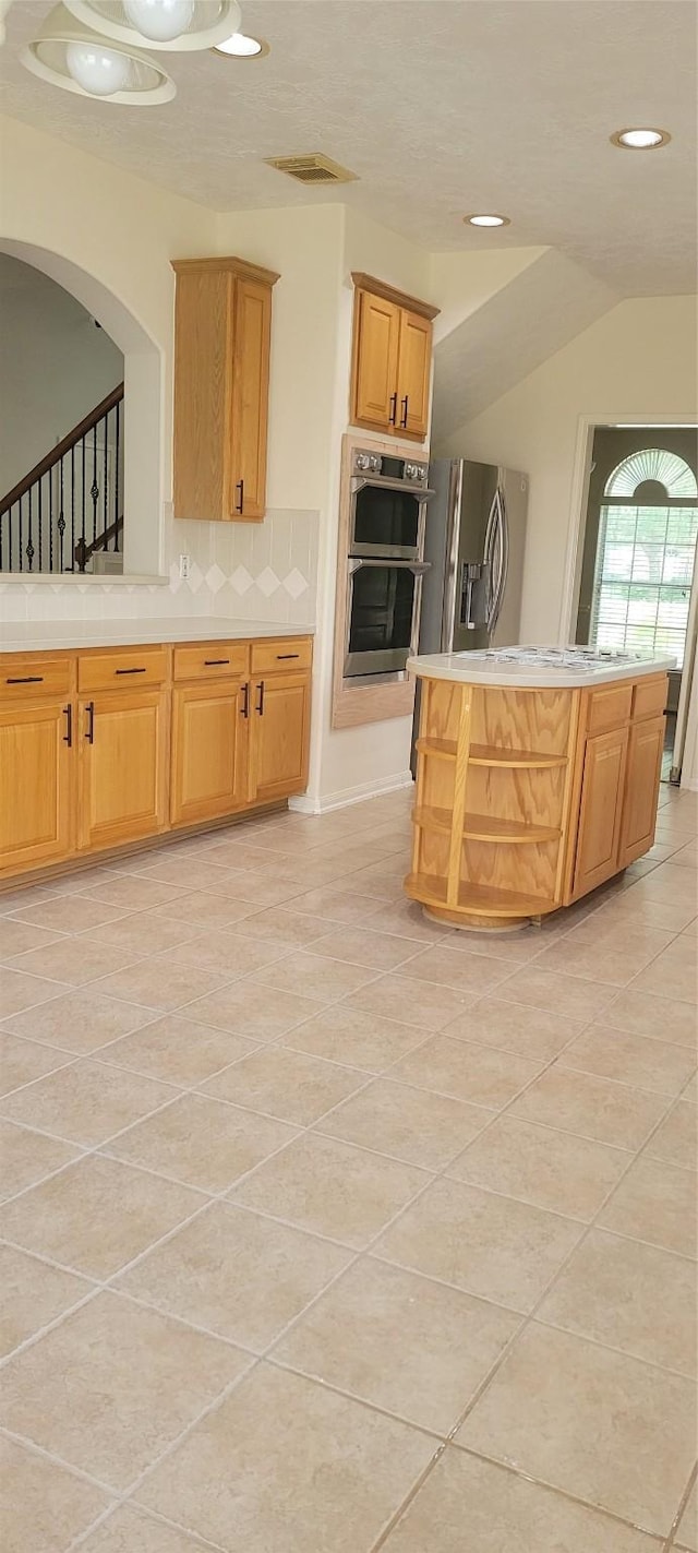 kitchen featuring a kitchen island, backsplash, light tile patterned floors, light countertops, and stainless steel appliances