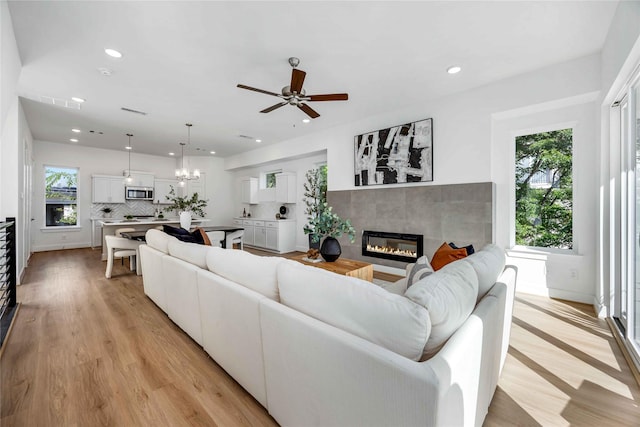 living room featuring ceiling fan with notable chandelier, recessed lighting, a fireplace, light wood finished floors, and baseboards