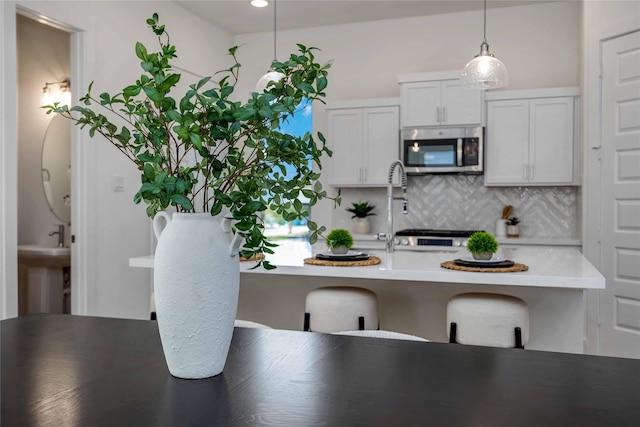 kitchen with a breakfast bar, pendant lighting, stainless steel microwave, light countertops, and decorative backsplash