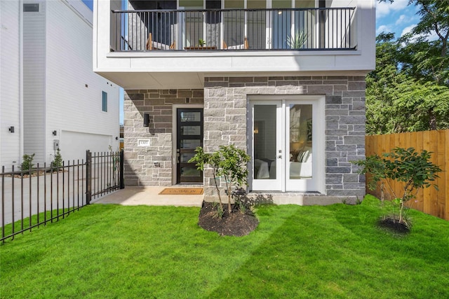 property entrance with a balcony, a yard, and stone siding