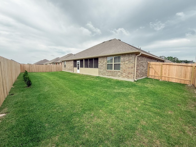 back of house with brick siding, a fenced backyard, a lawn, and roof with shingles