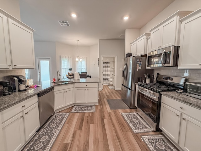 kitchen with appliances with stainless steel finishes, a sink, white cabinetry, light wood-type flooring, and backsplash