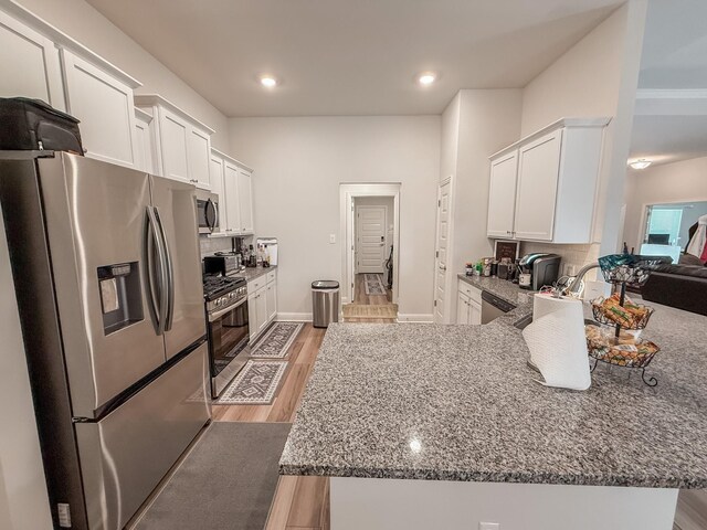 kitchen with dark stone counters, stainless steel appliances, white cabinetry, and light wood-style floors