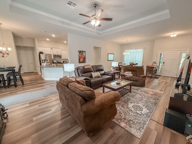living room featuring visible vents, a raised ceiling, ceiling fan with notable chandelier, and light wood-style floors