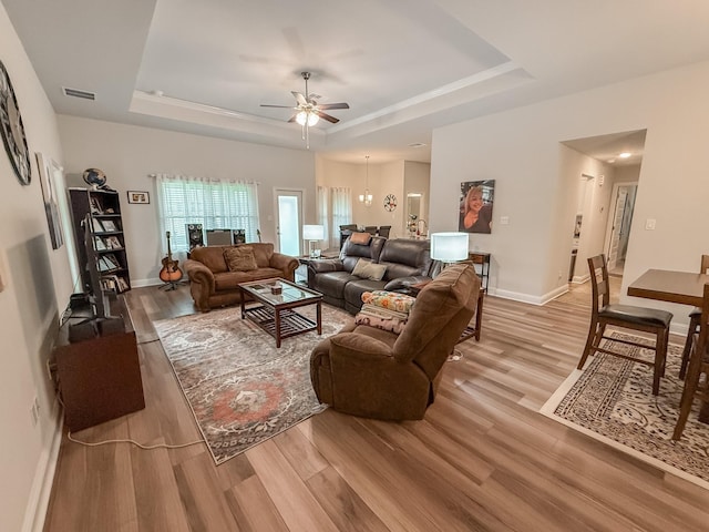 living area featuring visible vents, baseboards, ceiling fan, light wood-type flooring, and a raised ceiling