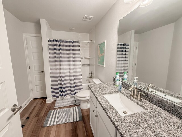 bathroom with visible vents, vanity, wood finished floors, toilet, and shower / tub combo