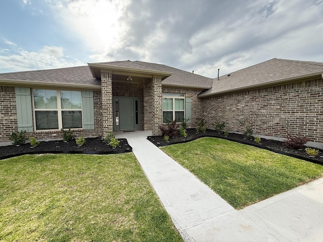 view of front of home featuring brick siding, a shingled roof, and a front yard