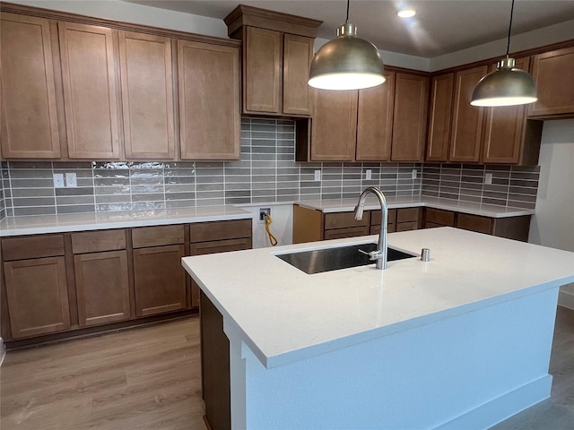 2223 Inglenook Grove Dr, Katy, TX 77493 - kitchen with decorative backsplash, light wood-style flooring, hanging light fixtures, a kitchen island with sink, and brown cabinets