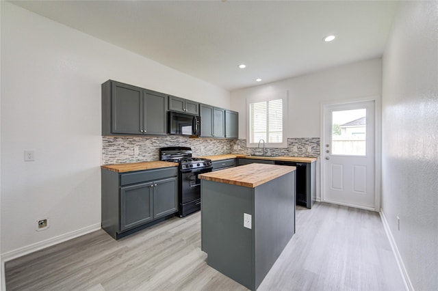 kitchen featuring backsplash, a sink, black appliances, light wood finished floors, and butcher block counters