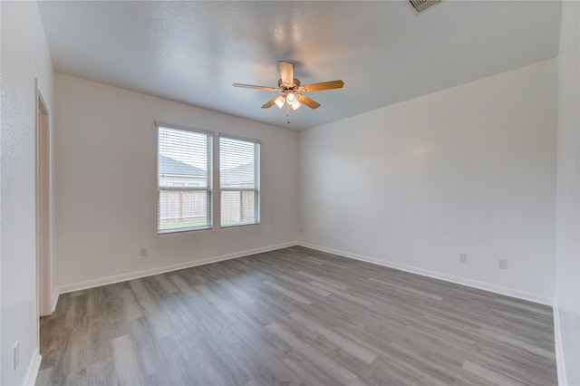 empty room with baseboards, a ceiling fan, wood finished floors, and visible vents
