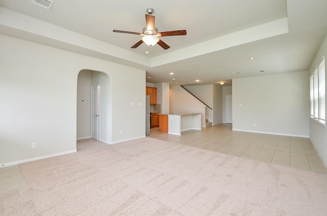 unfurnished living room featuring light tile patterned flooring, a ceiling fan, light colored carpet, and arched walkways