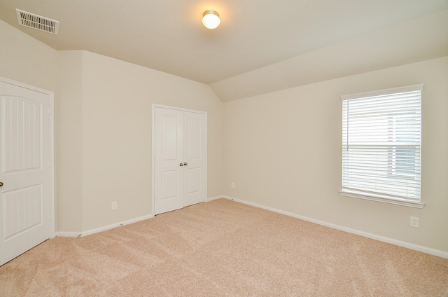 carpeted spare room with baseboards, vaulted ceiling, and visible vents