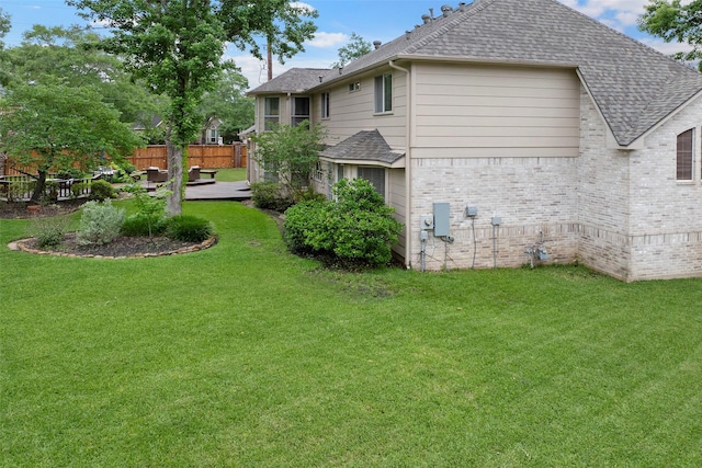 view of property exterior featuring a lawn, brick siding, fence, and roof with shingles