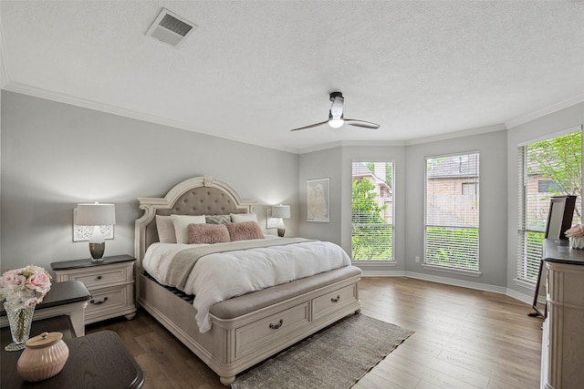 bedroom featuring a textured ceiling, ornamental molding, wood finished floors, and visible vents