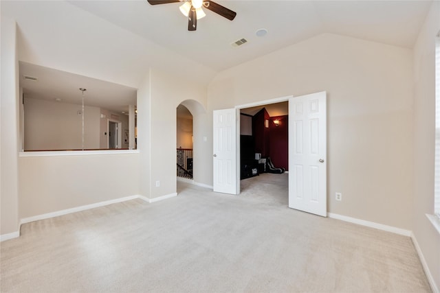 spare room featuring visible vents, lofted ceiling, ceiling fan, light colored carpet, and arched walkways