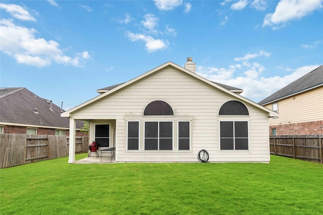 back of property with a fenced backyard, a patio, a chimney, and a lawn