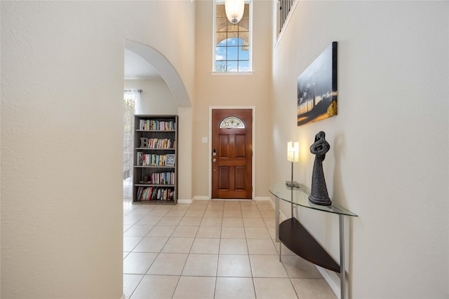 entryway with baseboards, arched walkways, a high ceiling, and light tile patterned floors