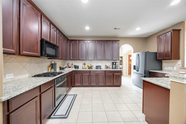 kitchen featuring backsplash, arched walkways, light stone countertops, and appliances with stainless steel finishes