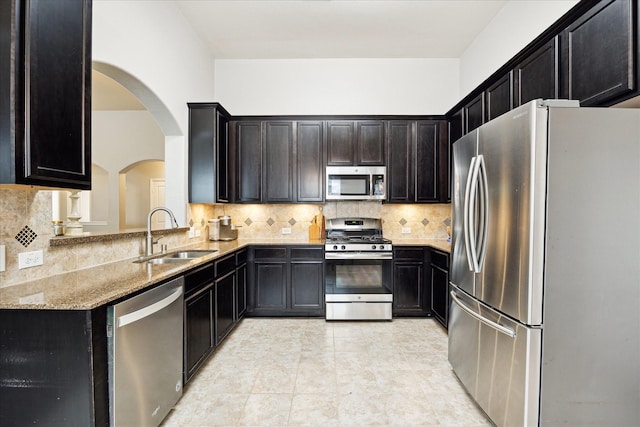 kitchen with light stone counters, a sink, arched walkways, stainless steel appliances, and tasteful backsplash