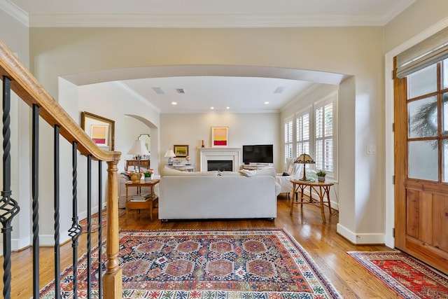living room with arched walkways, ornamental molding, and wood finished floors