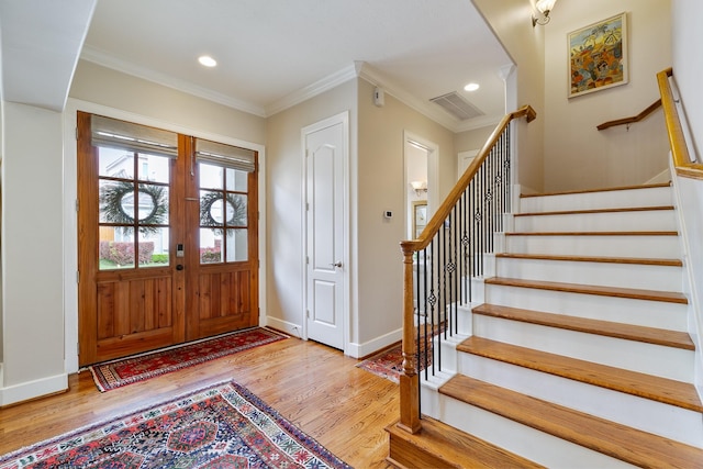 foyer featuring stairs, baseboards, wood finished floors, visible vents, and ornamental molding