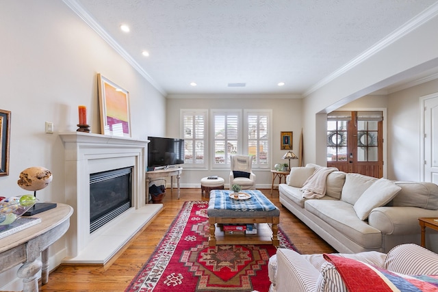 living area with crown molding, recessed lighting, a glass covered fireplace, and light wood-style flooring