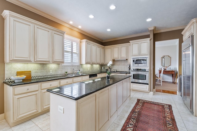 kitchen with cream cabinets, built in appliances, dark stone counters, tasteful backsplash, and a kitchen island