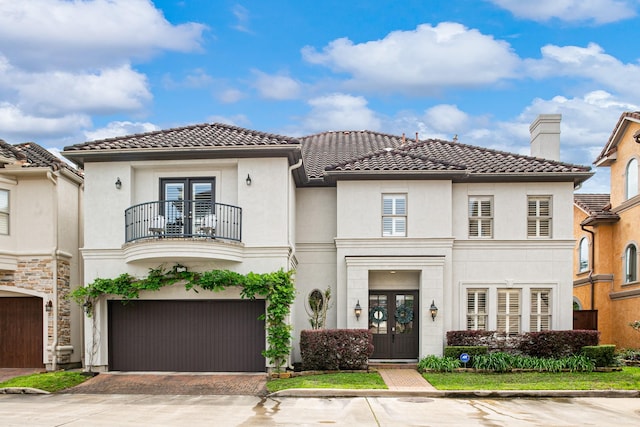 mediterranean / spanish-style home featuring a tiled roof, an attached garage, french doors, and a balcony