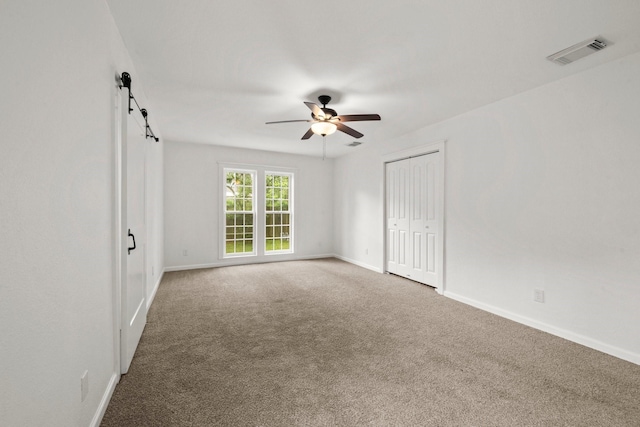 unfurnished room with ceiling fan, a barn door, carpet, baseboards, and visible vents