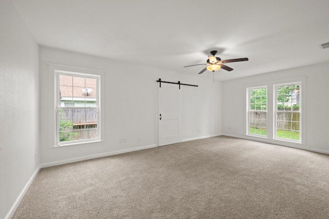 carpeted empty room with a ceiling fan, baseboards, visible vents, and a barn door
