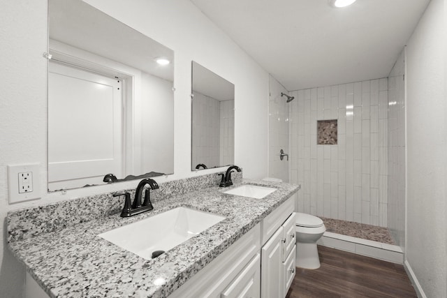 bathroom with double vanity, a sink, wood finished floors, and tiled shower