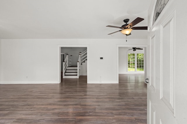 spare room featuring baseboards, stairs, ceiling fan, and dark wood-style floors