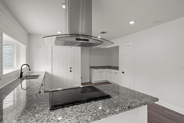 kitchen featuring island range hood, black electric cooktop, a sink, stone counters, and dark wood-type flooring