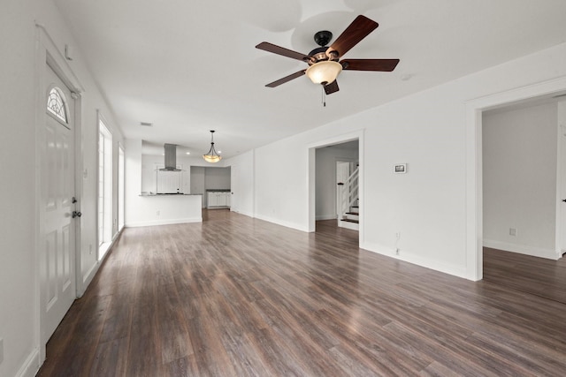 unfurnished living room featuring baseboards, a ceiling fan, stairs, and dark wood-style flooring