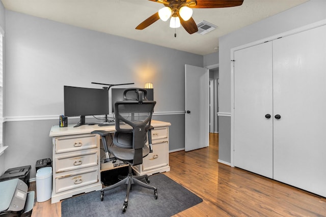 home office with baseboards, ceiling fan, wood finished floors, and visible vents