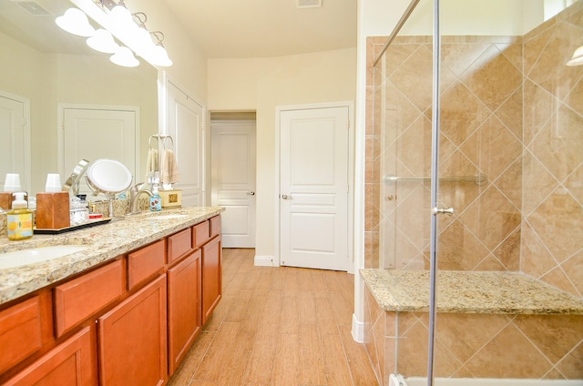 bathroom with a stall shower, visible vents, a sink, double vanity, and wood finished floors