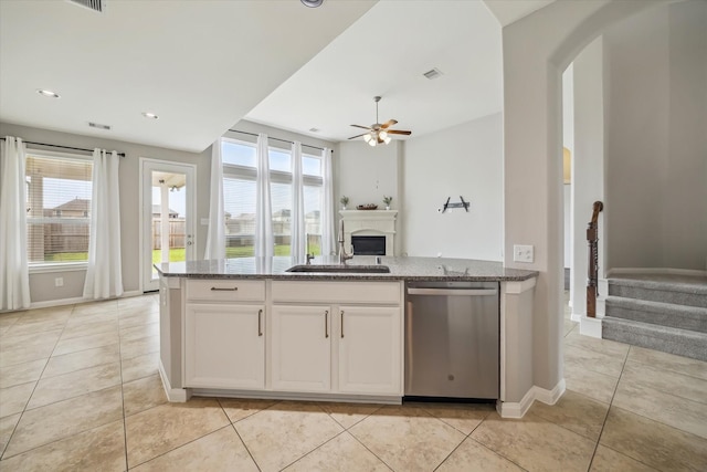 kitchen with stainless steel dishwasher, a sink, dark stone countertops, and plenty of natural light