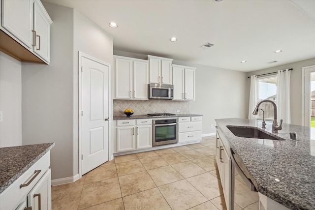 kitchen with white cabinets, a sink, dark stone counters, stainless steel appliances, and decorative backsplash