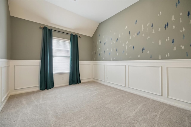 empty room featuring carpet floors, wainscoting, lofted ceiling, and a decorative wall
